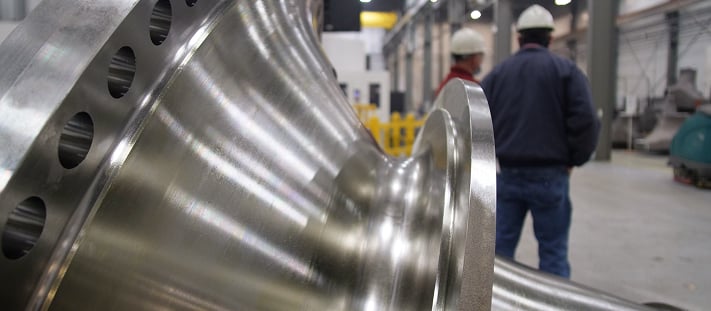 The shiny surface of a finished casting; two workers in the background.