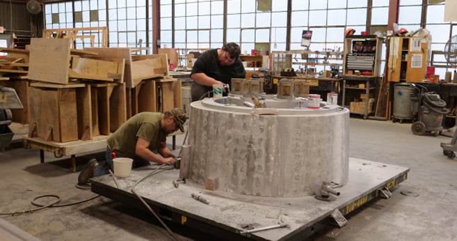 Two industrial workers examining a large metal casting mold at a steel foundry