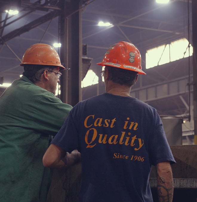Two workers in orange hard hats; one has a shirt that says "Cast in Quality Since 1906"