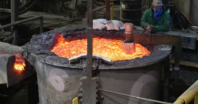 Molten steel rests in its ladle while a worker watches on.