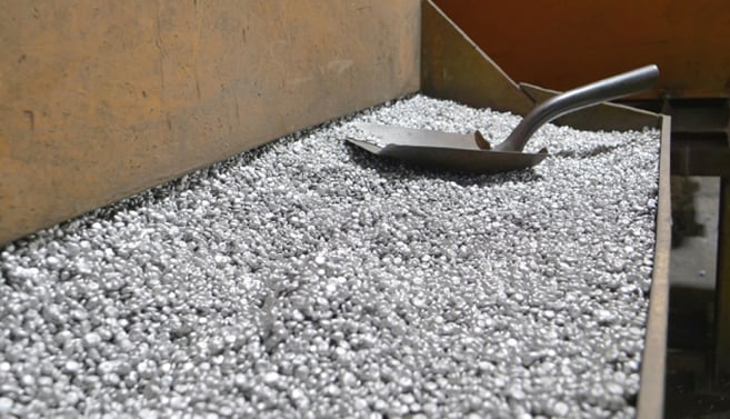 A metal shovel resting on foundry sand, a specialized silica-based material used for metal casting that resembles coarse gravel.