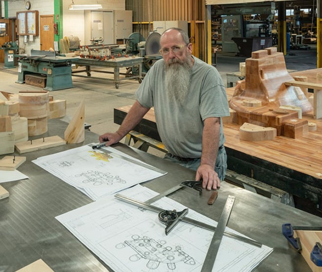 An employee who creates drawings for molds going over blueprints and schematics, with tools of his trade visible.