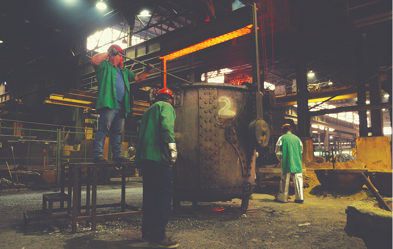 Three Harrison Steel employees tend to a ladel, a large bucket-shaped vessel used to transport and pour out molten metals.